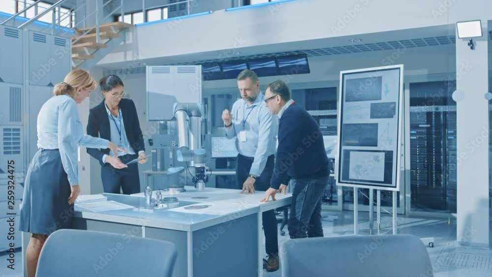 Poster Diverse Team of Industrial Robotics Engineers Gathered Around Table With Robot Arm, They Manipulate and Program it to Pick Up and Move Metal Component. Bright Facility, Creative People
