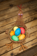Wicker basket in the form of a chicken with colored Easter eggs on a wooden background