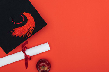 Top view of academic cap, diploma and apple on red surface