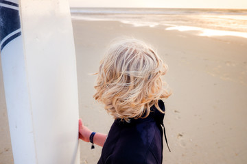 Junger Surfer steht mit Surfbrett am Strand und schaut Richtung Meer