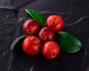 Cowberry (foxberry, lingonberry). Top view. Wild cranberry on dark rustic background. Ripe red forest berries Vaccinium vitis-idaea with green leaves. Copy space.