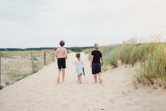 Drei Geschwister laufen am Strand über eine Sanddüne
