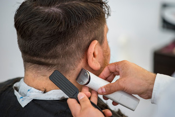 Client having his hair cut in a barber shop where the hair dresser is using a brush and a hair clipper on the mans back head.