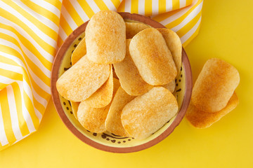 Potato chips in bowl on yellow background, top view