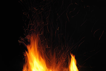 Flame of a burning fire with sparks in the night on a black background. Close-up