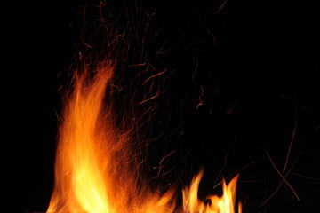 Flame of a burning fire with sparks in the night on a black background. Close-up