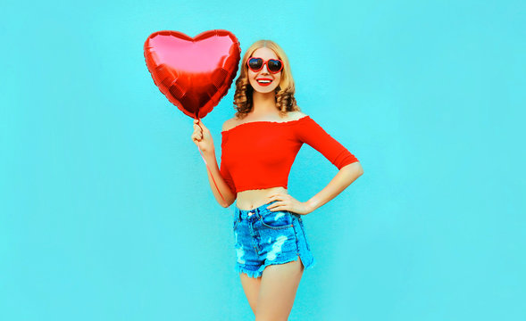 Portrait happy smiling woman holding red heart shaped air balloon on colorful blue background