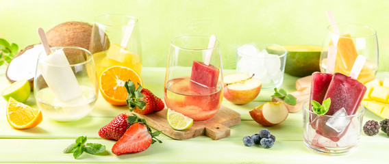 Selection of colourful ice pops and ingredients on green wood background