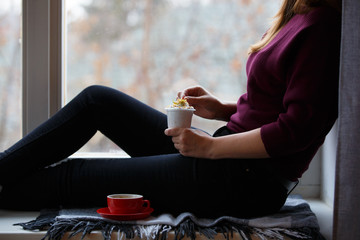 Young woman sitting near window and eating dessert
