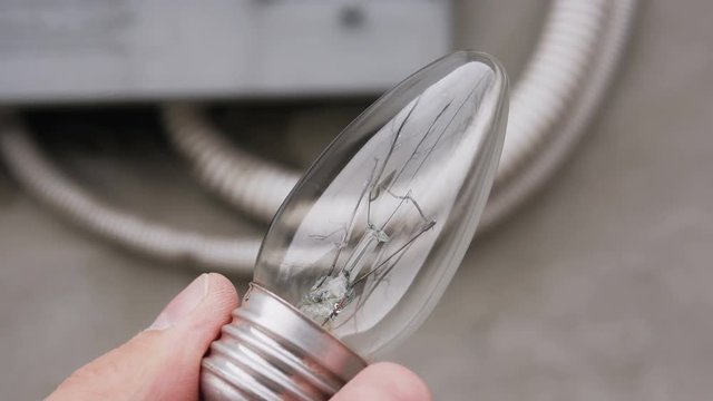 Closeup of a man's hand holding an incandescent lamp with burnt tungsten filament.