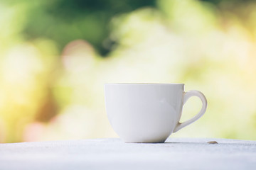 White coffee cup in garden bokeh background, vintage color
