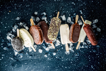 Assortment of various popsicle ice cream, vanilla and chocolate, with nuts, on a dark concrete...