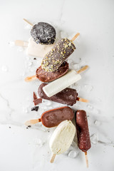 Assortment of various popsicle ice cream, vanilla and chocolate, with nuts, on a dark concrete background with ice, copy space top view