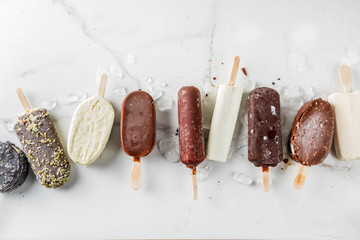 Assortment of various popsicle ice cream, vanilla and chocolate, with nuts, on a dark concrete...