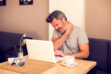 Man feeling neck pain while working with laptop
