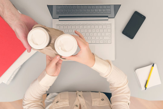 Man bringing coffee in paper cups to colleague woman