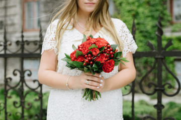 Hands of the bride hold a bouquet of red flowers