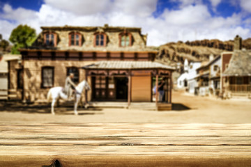 Wooden old table of free space for your decoration and wild west blurred background of big building and cowboy on horse. 