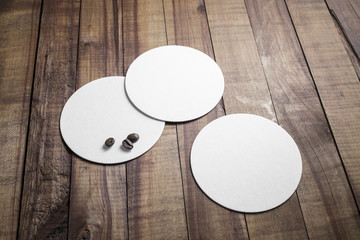 Three blank beer coasters and coffee beans on wooden background. Responsive design mockup.