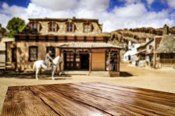 Wooden old table of free space for your decoration and wild west blurred background of big building and cowboy on horse. 