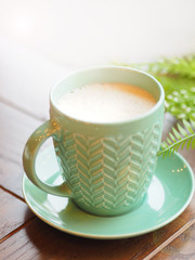 Porcelain aquamarine colored cup with cappuccino. Coffee mug on wooden table. Tasty hot beverage.