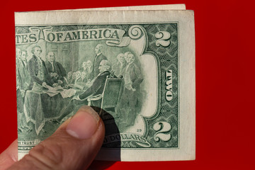 A two-dollar bill in a man's hand against a red background.