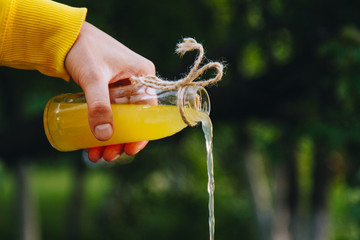 male hand pours homemade lemonade from a bottle on a background of trees on the nature outdoors. close-up, healthy food, diet, proper nutrition, picnic. Summer.