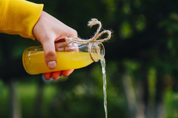 male hand pours homemade lemonade from a bottle on a background of trees on the nature outdoors. close-up, healthy food, diet, proper nutrition, picnic. Summer.