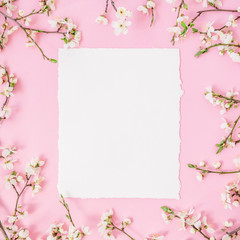 Floral frame with white flowers and card on pastel pink background. Flat lay, top view.