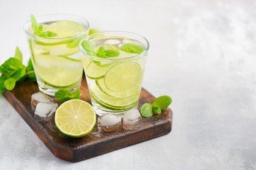 Cold refreshing summer drink with lime and mint in a glass on a gray concrete or stone background.