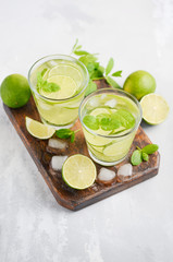 Cold refreshing summer drink with lime and mint in a glass on a gray concrete or stone background.