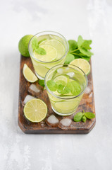 Cold refreshing summer drink with lime and mint in a glass on a gray concrete or stone background.