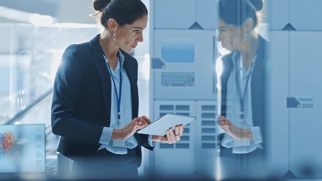 Stylish Female Industrial Robotics Engineer Uses Tablet Computer to Program and Manipulate Robot Arm for Lifting, Moving Objects. Technology Research Facility for Machine Learning and Cloud Computing