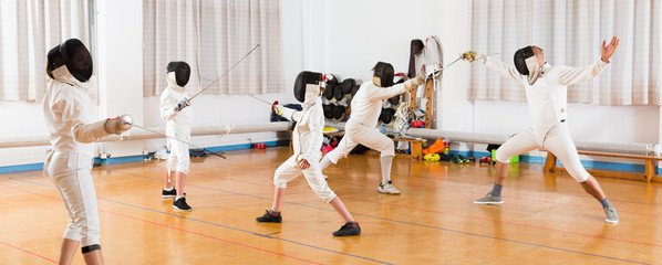 Adults and teens wearing fencing uniform practicing with foil