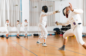 Coaches demonstrating to young athletes attack movements with rapier during fencing workout