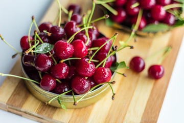 A handful of ripe red cherries in a metal can on a white background with green leaves