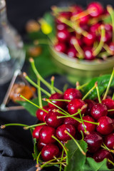 A handful of ripe red cherries in a metal can on a black background with green leaves