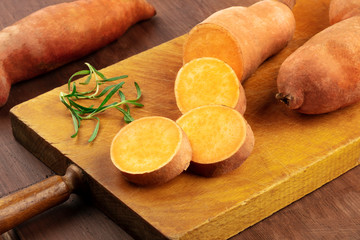 A closeup photo of slices of sweet potatoes with branches of fresh rosemary, on a vintage wooden cutting board