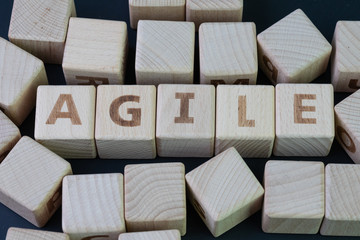 Agile software development concept, cube wooden block with alphabet building the word Agile at the center on dark blackboard background, requirements and solutions evolve through collaborative effort