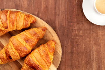 A closeup of a breakfast with croissants and coffee, shot from above forming a frame on a dark rustic wooden background with copy space