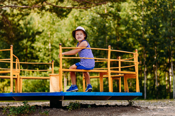seven-year-old cheerful boy in a striped t-shirt and hat sitting on a yellow children's carousel