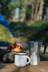 Mockup of metal camping aluminum cup or mug and coffee maker near bonfire on background tent. Concept adventures and nomad lifestyle