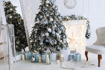 Close up photo of Christmas interior with white and blue color of a bright stylish living room with gifts, fireplace, Christmas tree and candles