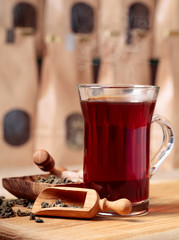 Glass of hot tea and wooden spoon with dried tea leaves.