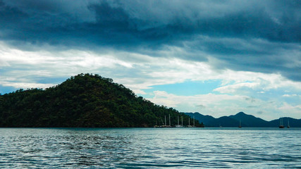 bad weather over the island, dark gray clouds, yachts, a beautiful and green island in the sea or...