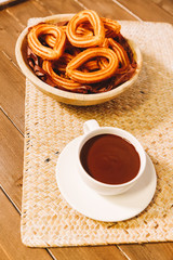 spanish fritters served on a wooden table with a cup of hot chocolate