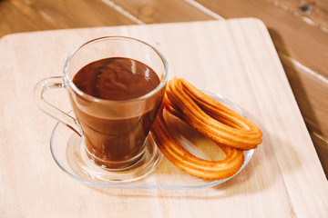 a glass cup with hot chocolate and two spanish fritters served on a wooden board