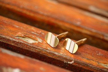 Man's golden cuff links on a wooden bench, selective focus