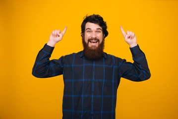 Fototapeta premium Happy bearded man pointing up with both hands on yellow background.