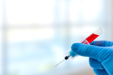 Doctor, or surgeon s hand in a blue medical glove holds a syringe with blood , conceptual image on white background copy text